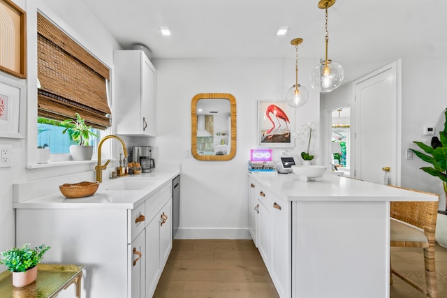 kitchen featuring sink, light wood-type flooring, white cabinets, and decorative light fixtures