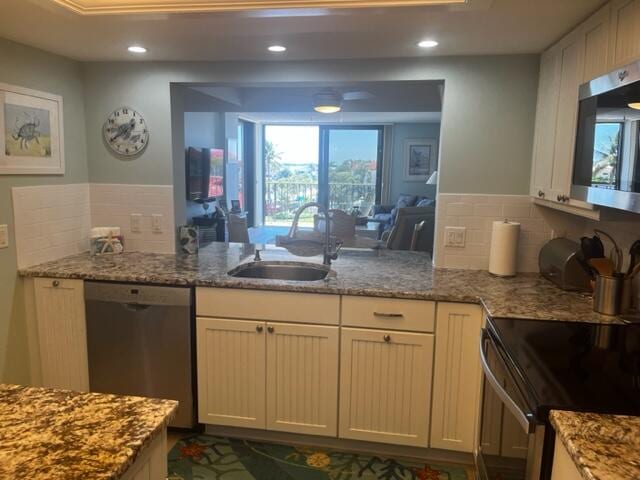 kitchen featuring stainless steel appliances, light stone countertops, kitchen peninsula, backsplash, and sink