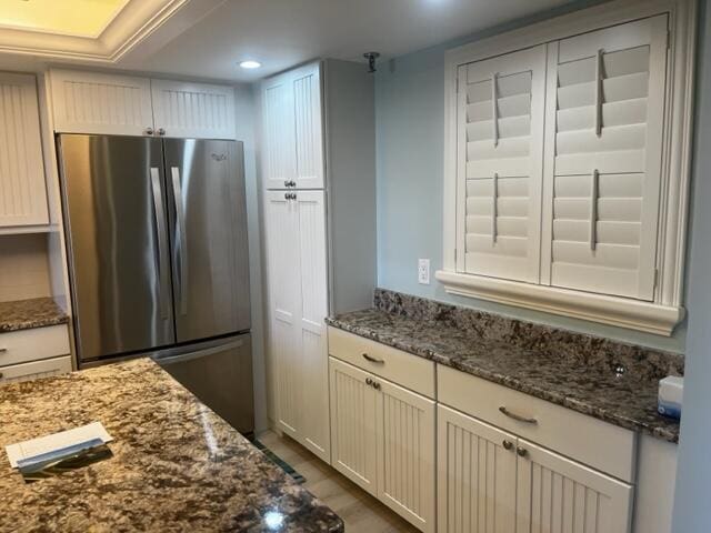 kitchen with dark stone counters, stainless steel refrigerator, and white cabinetry