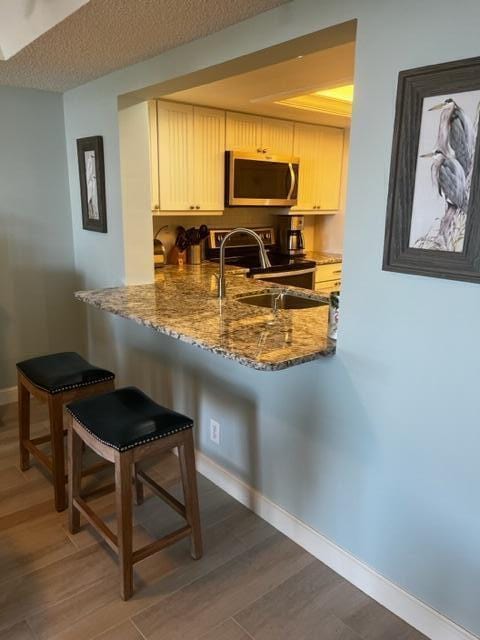 kitchen featuring dark hardwood / wood-style floors, a kitchen bar, dark stone countertops, and electric range oven