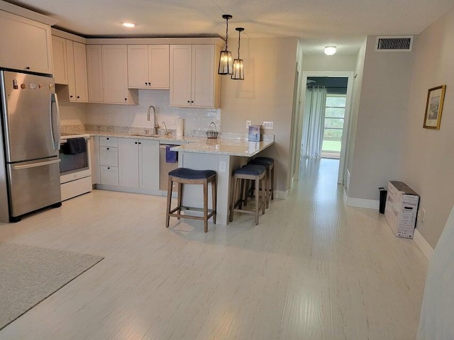 kitchen with white cabinets, sink, appliances with stainless steel finishes, kitchen peninsula, and a breakfast bar area