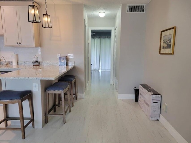 kitchen with kitchen peninsula, light stone countertops, decorative light fixtures, a kitchen bar, and white cabinetry