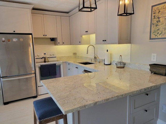 kitchen with sink, white electric range, stainless steel fridge, pendant lighting, and a breakfast bar