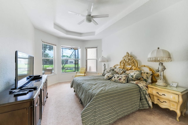 carpeted bedroom featuring a tray ceiling, baseboards, and ceiling fan