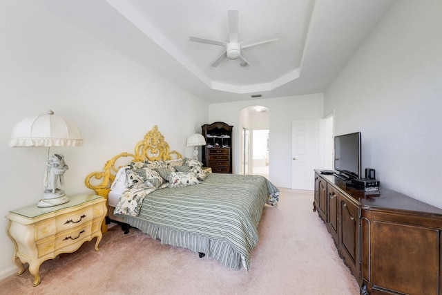 bedroom with light carpet, connected bathroom, arched walkways, a raised ceiling, and ceiling fan