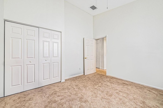 unfurnished bedroom with a towering ceiling, light carpet, and a closet