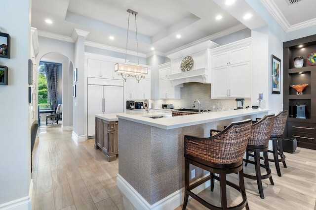 kitchen featuring a tray ceiling, a breakfast bar, light hardwood / wood-style flooring, and white cabinetry