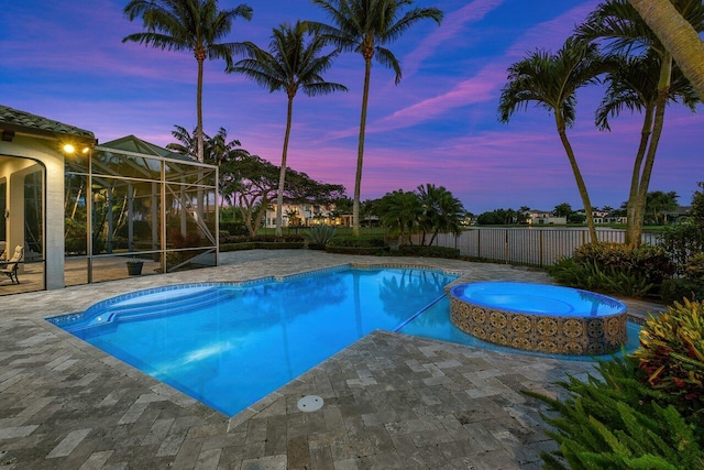 pool at dusk with glass enclosure, an in ground hot tub, and a patio