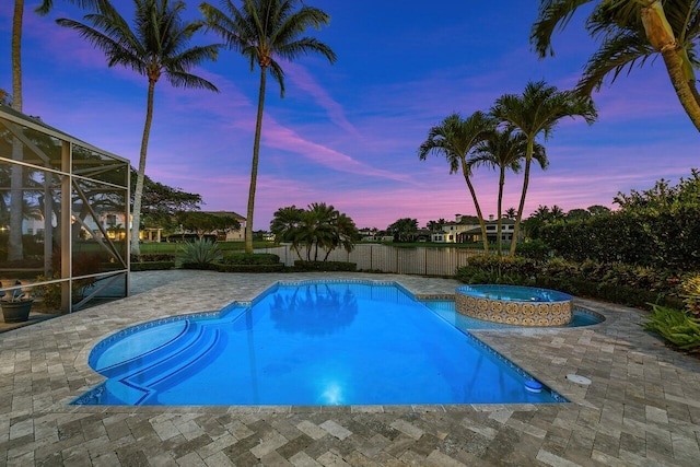 pool at dusk featuring an in ground hot tub, glass enclosure, and a patio