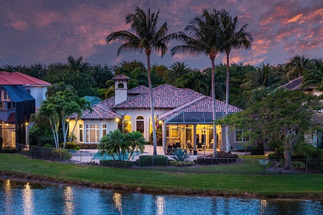 back house at dusk with a lawn, a patio area, and a water view