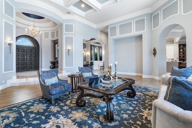 living room featuring coffered ceiling, crown molding, a chandelier, and light hardwood / wood-style floors