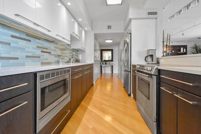 kitchen with white cabinetry, sink, stainless steel appliances, light hardwood / wood-style flooring, and tasteful backsplash