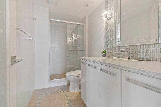 bathroom with tile flooring, tile walls, a shower with shower door, vanity, and toilet