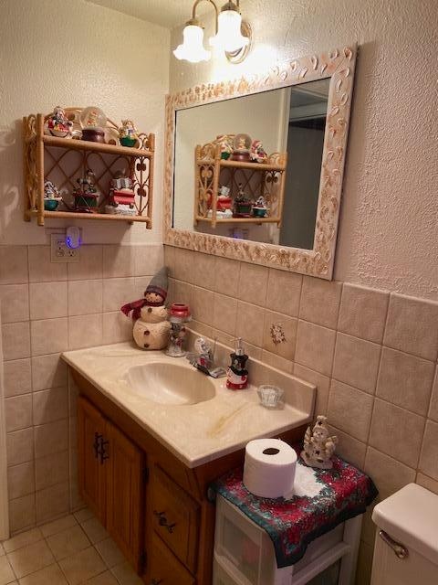 bathroom featuring tile floors, vanity, toilet, and tile walls