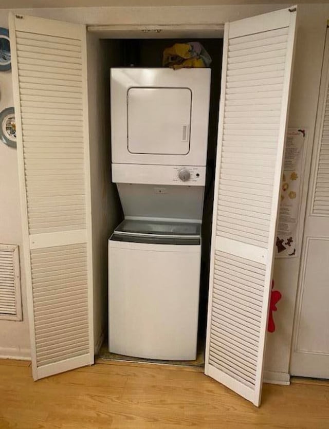 laundry area with light hardwood / wood-style floors and stacked washing maching and dryer