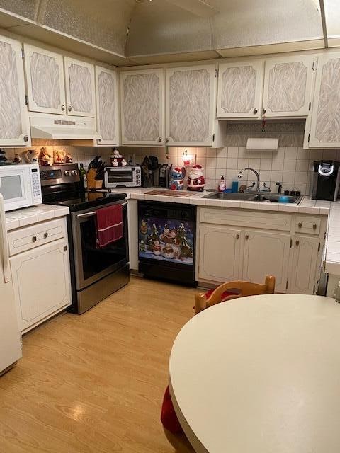 kitchen featuring electric range, light hardwood / wood-style flooring, tile counters, and dishwashing machine