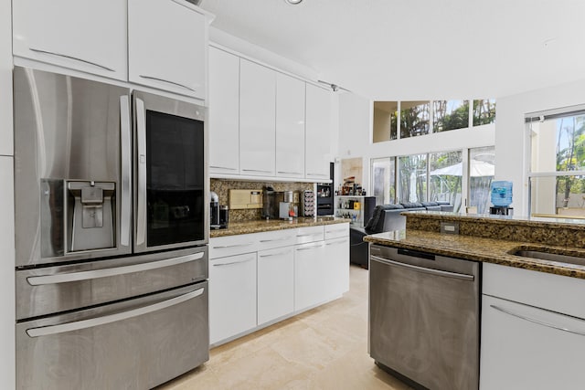 kitchen with white cabinets, stainless steel appliances, light tile floors, and dark stone counters