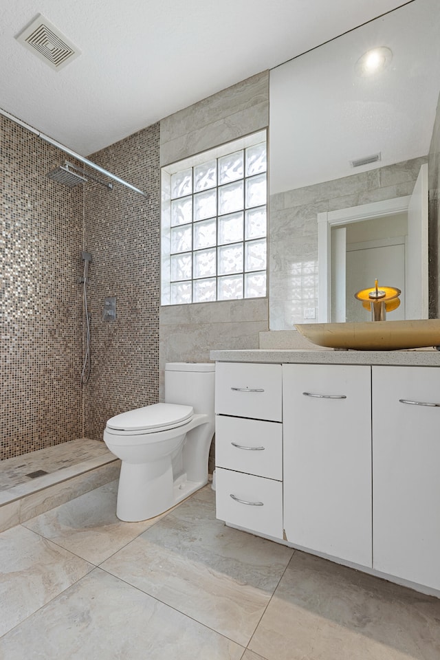 bathroom with tile walls, toilet, tiled shower, tile floors, and vanity