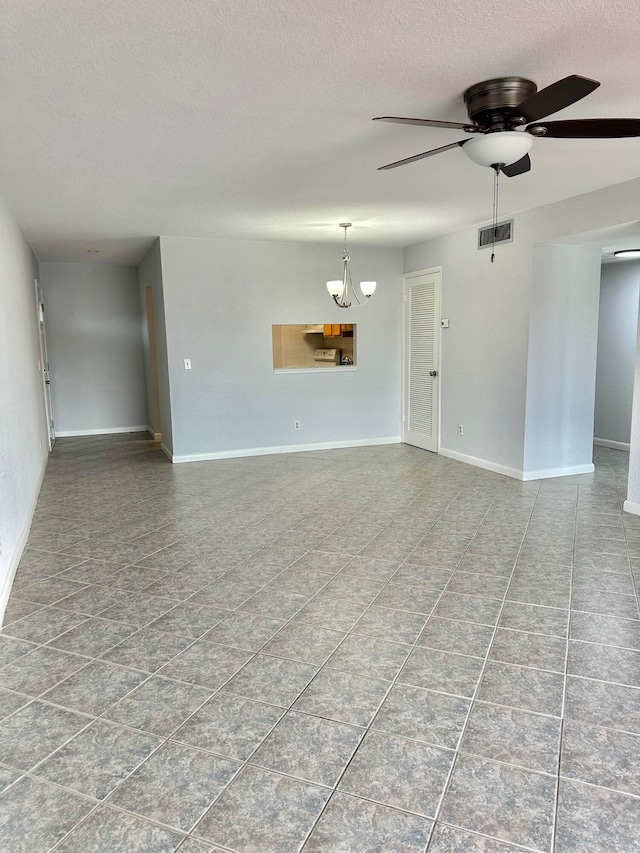 empty room featuring tile flooring, ceiling fan with notable chandelier, and a textured ceiling