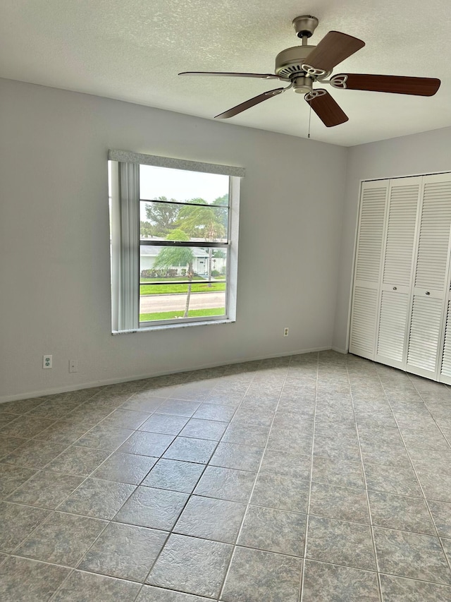 unfurnished bedroom with a closet, ceiling fan, light tile floors, and a textured ceiling