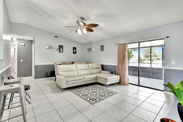 living room featuring ceiling fan, vaulted ceiling, light tile floors, and a textured ceiling