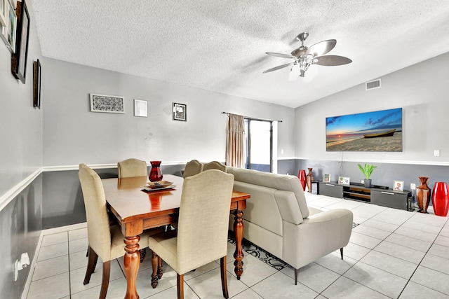 dining space with ceiling fan, vaulted ceiling, light tile flooring, and a textured ceiling