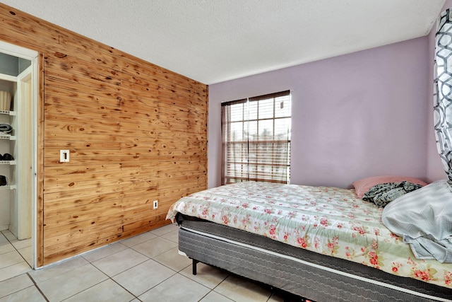 bedroom featuring a textured ceiling, wood walls, and light tile floors