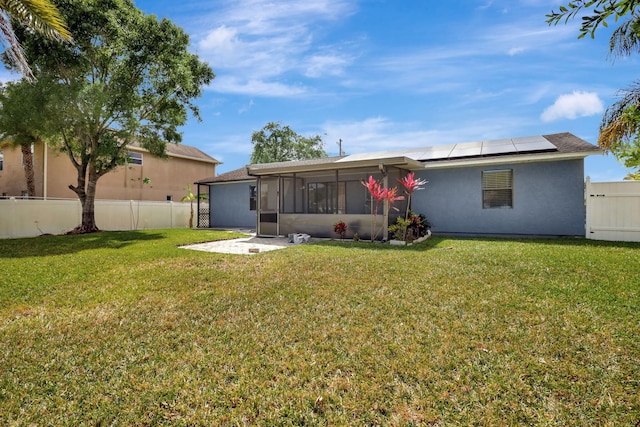 rear view of property featuring a lawn, solar panels, and a sunroom