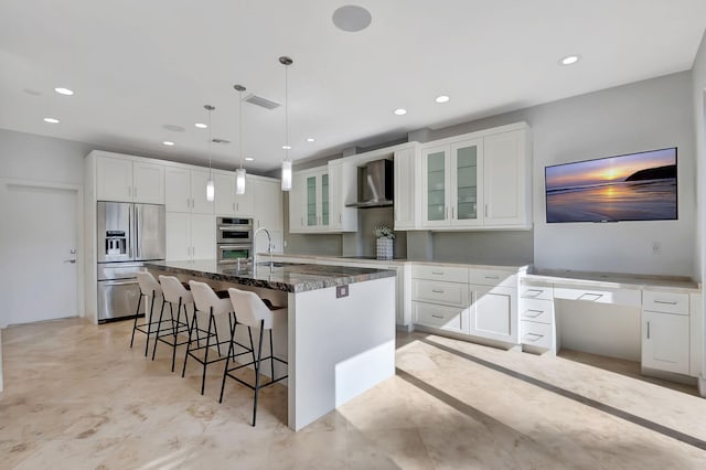 kitchen featuring white cabinets, appliances with stainless steel finishes, a kitchen island with sink, and wall chimney exhaust hood