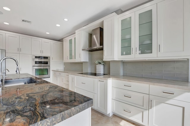 kitchen with tasteful backsplash, wall chimney exhaust hood, stainless steel double oven, sink, and white cabinets