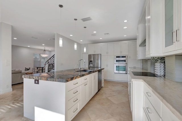 kitchen featuring appliances with stainless steel finishes, sink, a large island with sink, dark stone countertops, and white cabinets