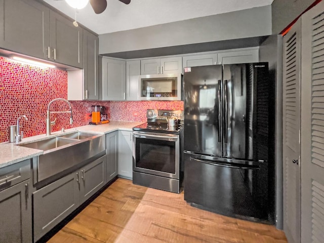 kitchen with appliances with stainless steel finishes, ceiling fan, light hardwood / wood-style flooring, gray cabinets, and backsplash