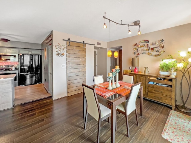 dining space with dark hardwood / wood-style floors, track lighting, and a barn door