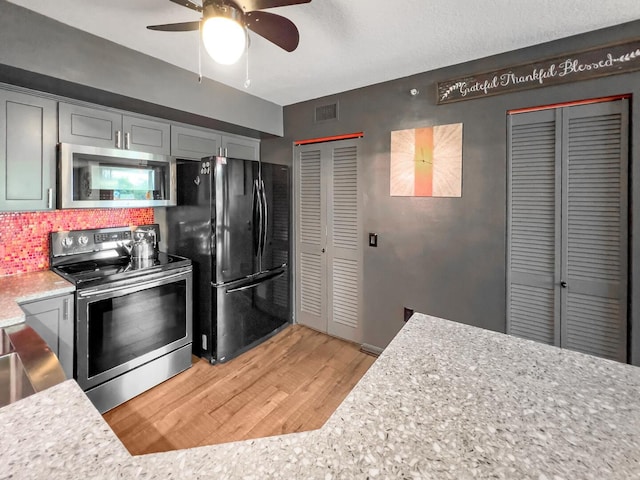 kitchen with ceiling fan, appliances with stainless steel finishes, light stone counters, tasteful backsplash, and hardwood / wood-style flooring