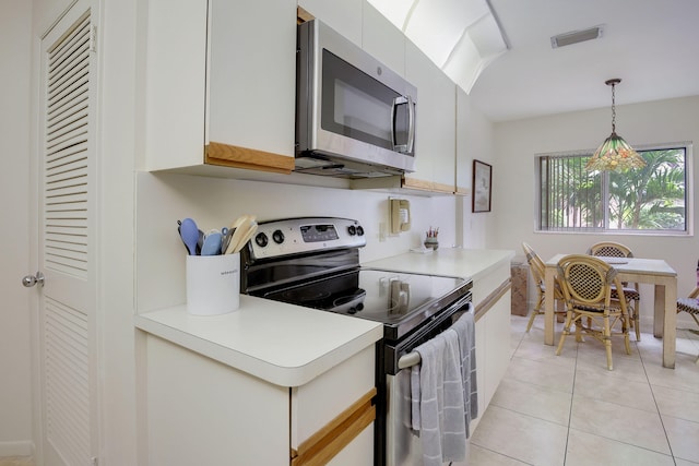 kitchen featuring appliances with stainless steel finishes, hanging light fixtures, light tile flooring, white cabinetry, and a notable chandelier