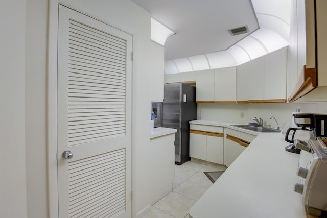 kitchen with white cabinetry, stainless steel fridge, sink, and light tile flooring