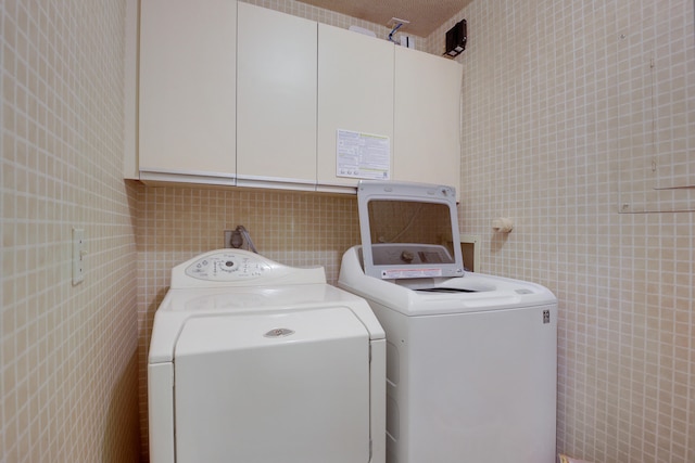 laundry room featuring tile walls, washer and clothes dryer, electric dryer hookup, and cabinets