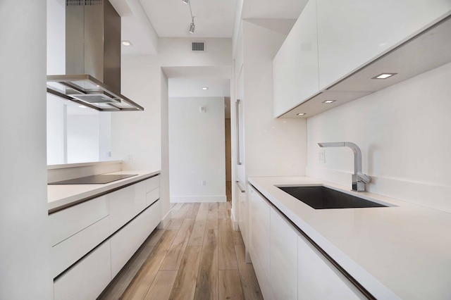 kitchen featuring white cabinetry, island range hood, rail lighting, and sink