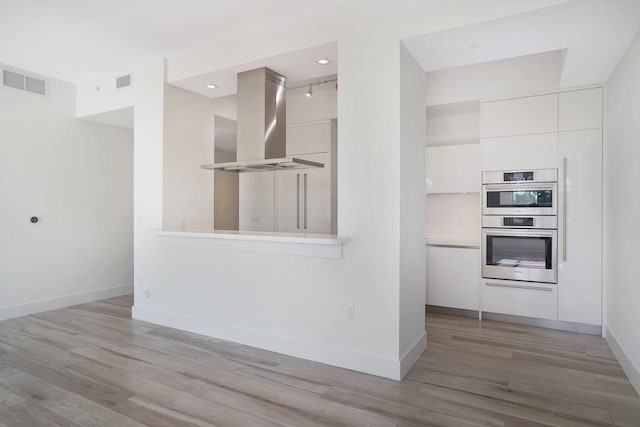 kitchen featuring white cabinetry, island exhaust hood, stainless steel double oven, and light hardwood / wood-style flooring