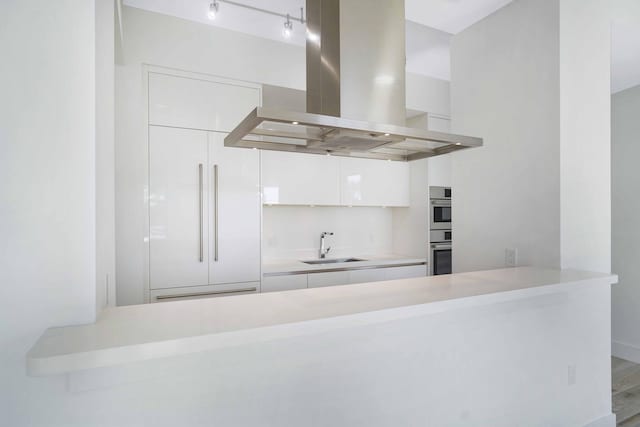 kitchen with sink, wood-type flooring, white cabinets, island exhaust hood, and stainless steel double oven