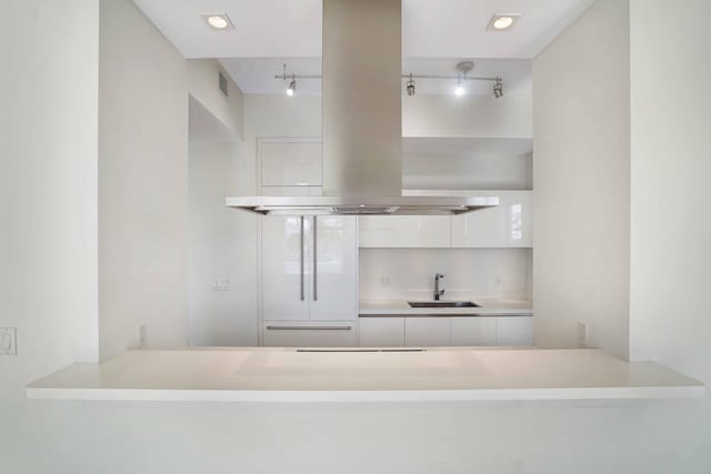 kitchen with white cabinetry, sink, and island range hood