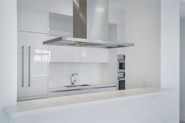 kitchen with sink, island range hood, white cabinets, and stainless steel double oven