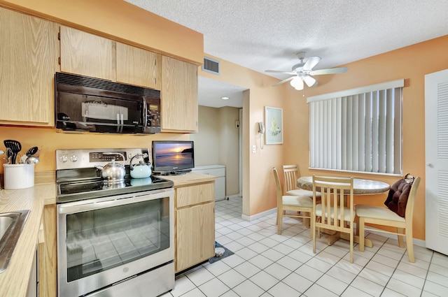 kitchen featuring stainless steel electric range, light tile patterned floors, a textured ceiling, and light brown cabinetry