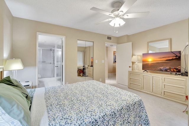 bedroom featuring ceiling fan, ensuite bathroom, a textured ceiling, light carpet, and a closet