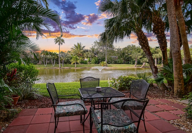 patio terrace at dusk featuring a water view and a yard