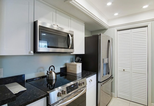 kitchen featuring stainless steel appliances, light tile floors, ornamental molding, white cabinets, and dark stone countertops