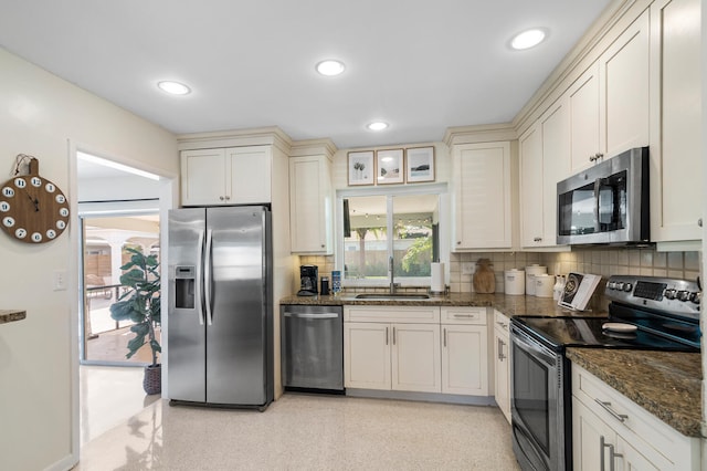 kitchen with decorative backsplash, appliances with stainless steel finishes, glass insert cabinets, a sink, and dark stone counters