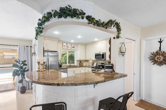 kitchen with dark stone counters, glass insert cabinets, a breakfast bar, appliances with stainless steel finishes, and a sink