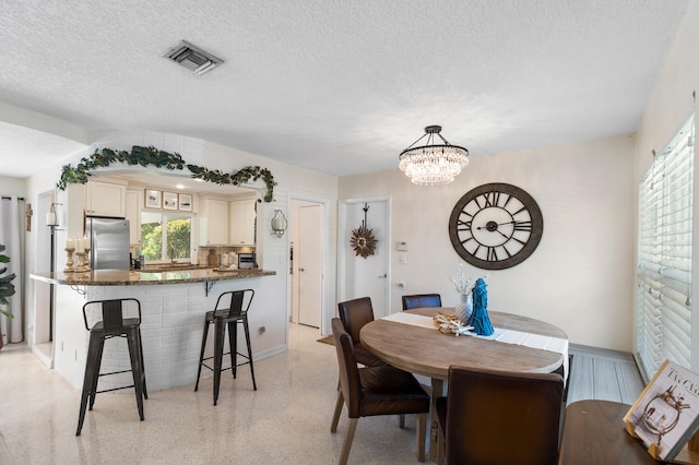 dining area featuring visible vents, light speckled floor, a textured ceiling, and a chandelier