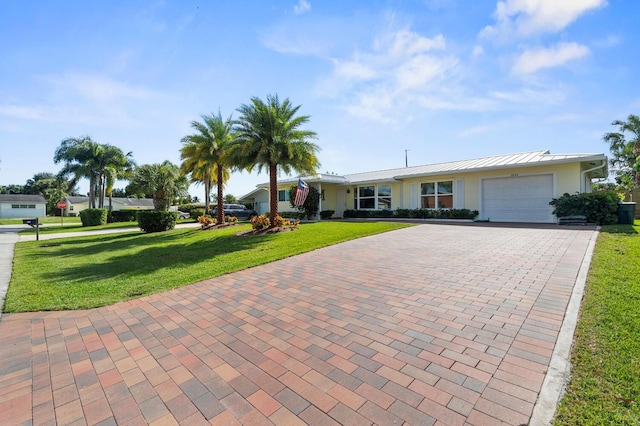 single story home with a garage, metal roof, a standing seam roof, decorative driveway, and a front lawn